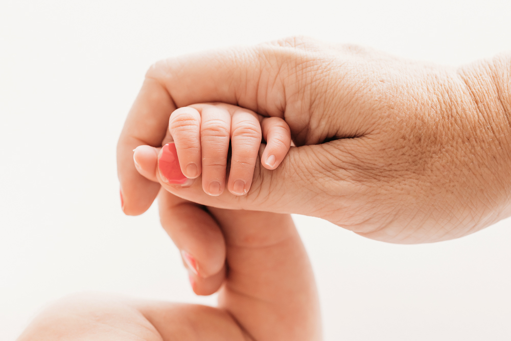 Newborns tiny hand clutching mothers finger in tender close-up at Reflection Images by Tracy Rowell in Florence SC.