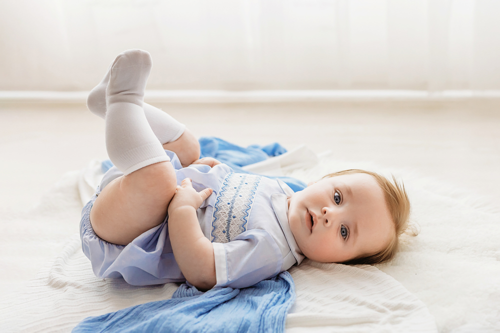 Smiling baby lying on white blanket with blue wrap, professional photography near Florence SC