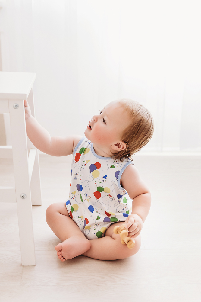 Levi seated on the floor holding a wooden toy, reaching toward a small white stool in soft window light at Reflection Images by Tracy Rowell in Florence SC