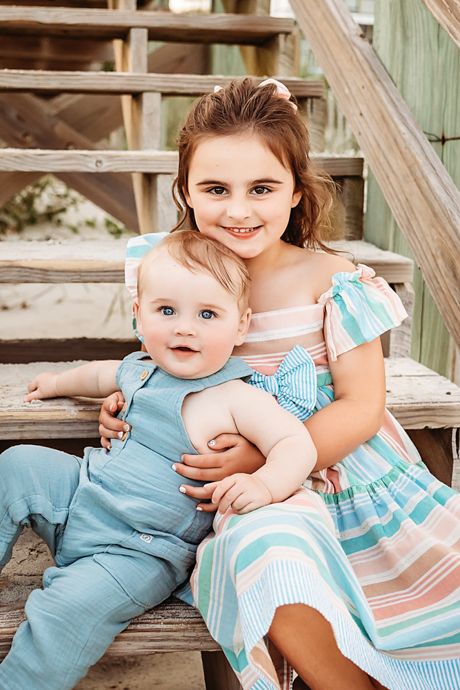 Stella holding baby Cole on beach stairs with sweet smiles and pastel outfits at Reflection Images by Tracy Rowell in Florence SC