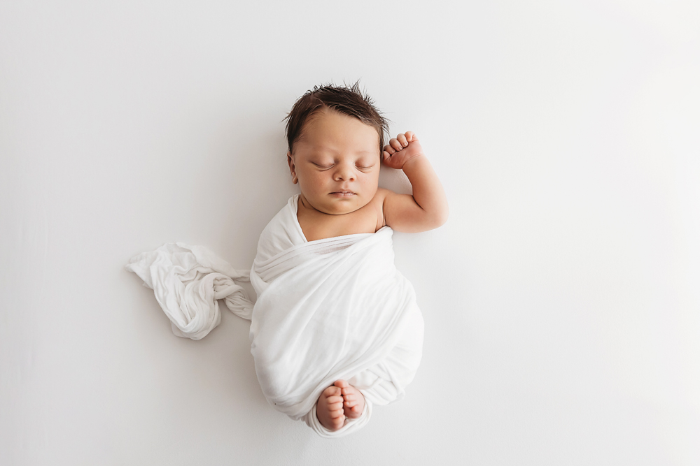 Newborn Liston lying on white blanket with one arm up and white wrap loosely draped at Reflection Images by Tracy Rowell in Florence SC