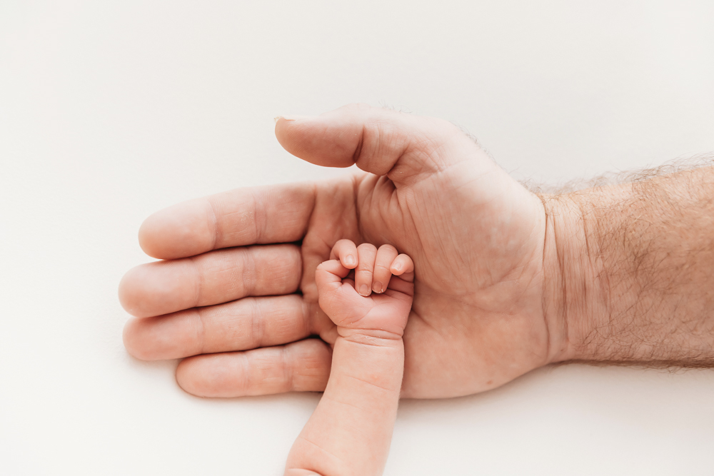 Close-up of newborns tiny hand resting in dads palm at Reflection Images by Tracy Rowell in Florence SC.
