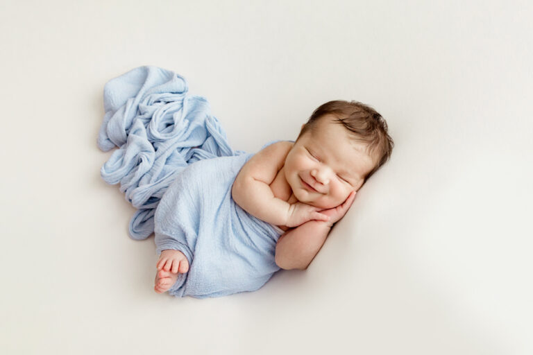 Baby Finn wrapped in soft blue, side-lying with a sweet smile at Reflection Images by Tracy Rowell in Florence SC