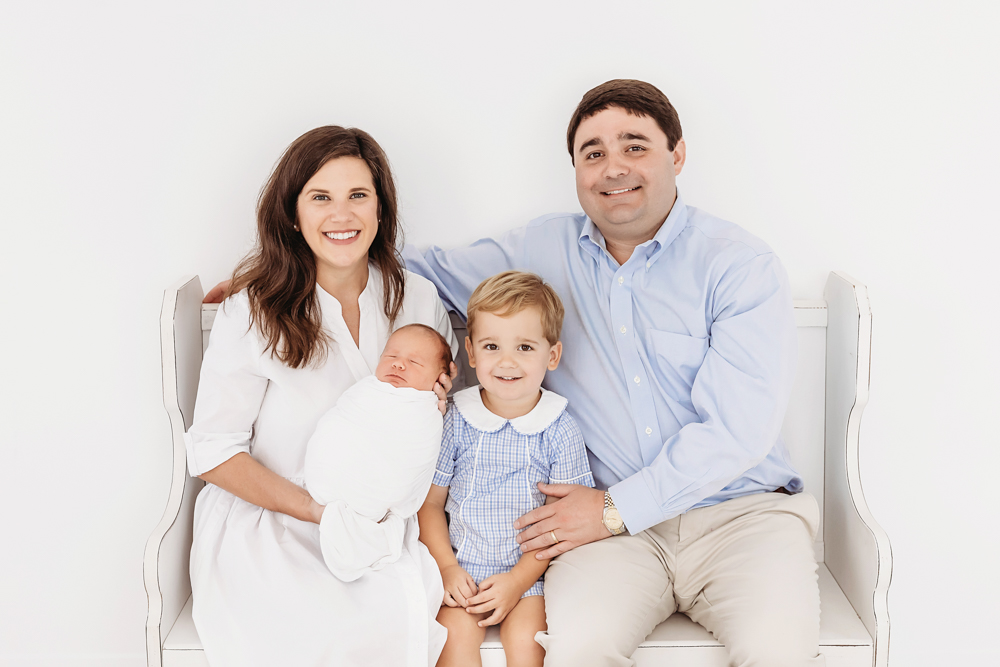 Rhett and Eliza Spencer seated on a white bench with sons Tommy and swaddled baby Harry at Reflection Images by Tracy Rowell in Florence SC
