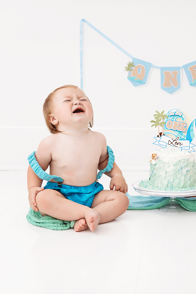 Levi crying joyfully beside his ocean-themed birthday cake and 'ONE' banner while wearing blue bloomers at Reflection Images by Tracy Rowell in Florence SC