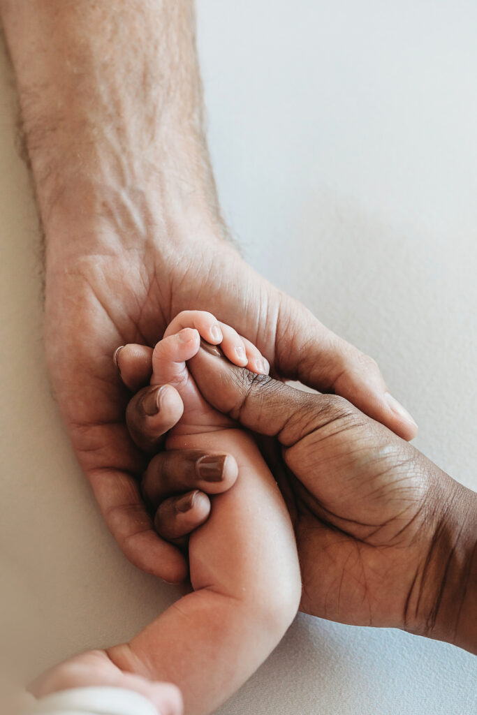 Mom and dad both holding newborn's tiny hand together on a soft white background at Reflection Images by Tracy Rowell in Florence SC