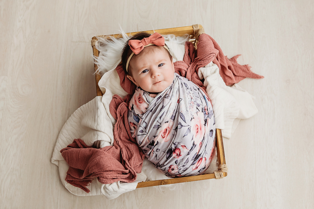 Mary Katherine in a floral swaddle with dusty rose layers resting in a wooden box on wood floor at Reflection Images by Tracy Rowell in Florence SC
