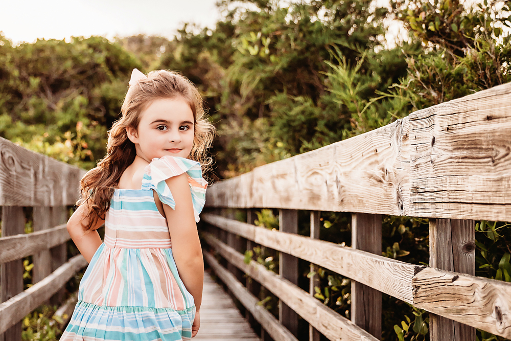 Stella looking back with flowing curls and a white bow on a coastal boardwalk at Reflection Images by Tracy Rowell in Florence SC
