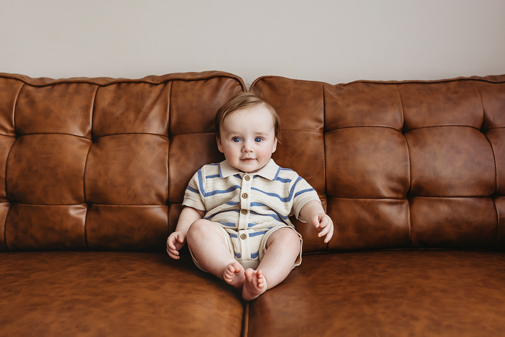 Baby sitting in cream-and-blue striped romper on leather couch, newborn photographer near Florence SC