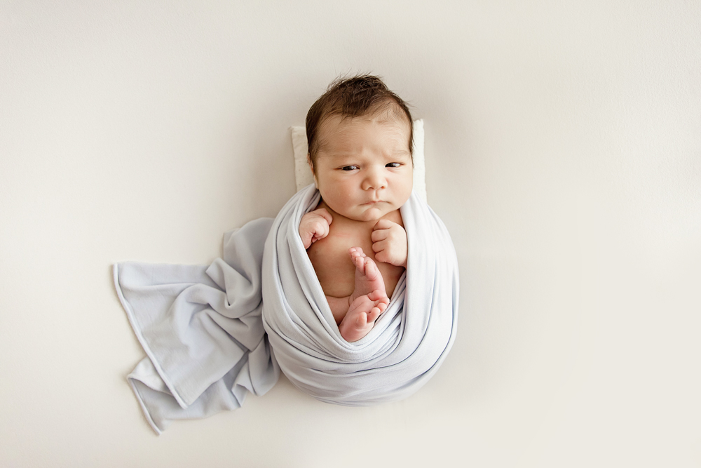 Newborn Finn sitting upright in blue wrap, looking curiously at camera at Reflection Images by Tracy Rowell in Florence SC