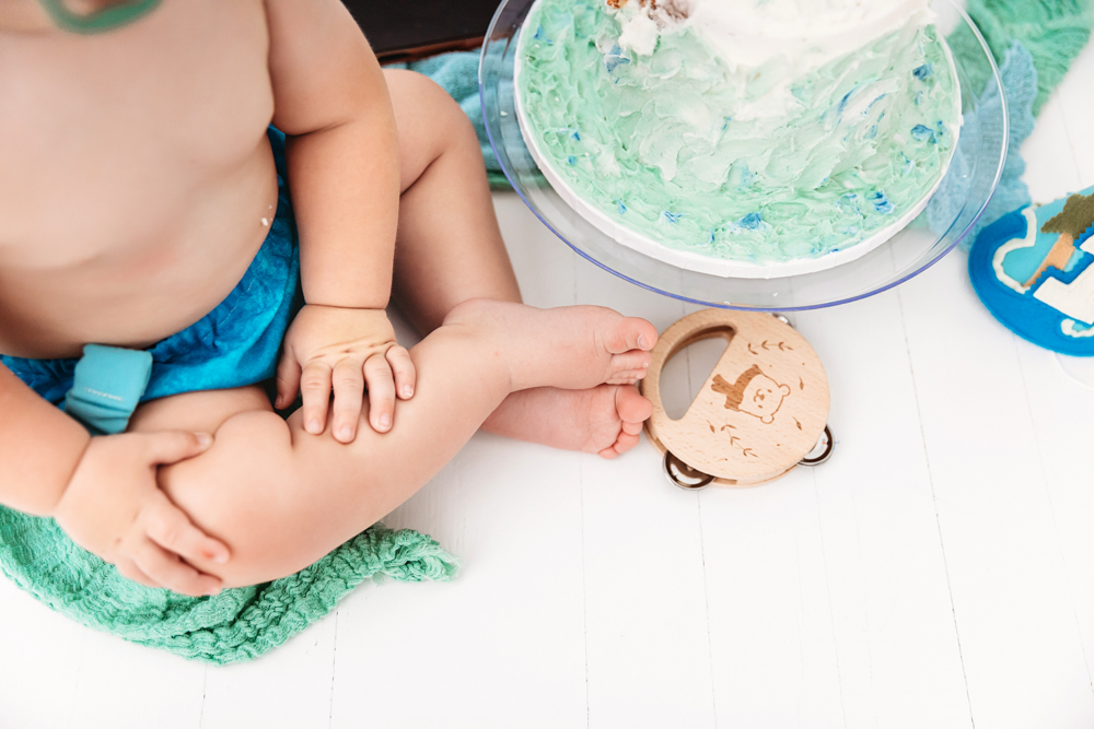 Close-up of Levis hands and feet near a light blue smash cake with a bear tambourine on the white floor at Reflection Images by Tracy Rowell in Florence SC