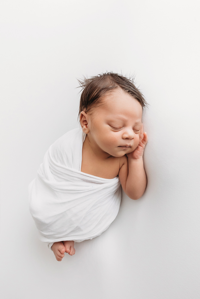 Full body view of newborn Liston swaddled in white and posed on his side with cheek resting on hand at Reflection Images by Tracy Rowell in Florence SC