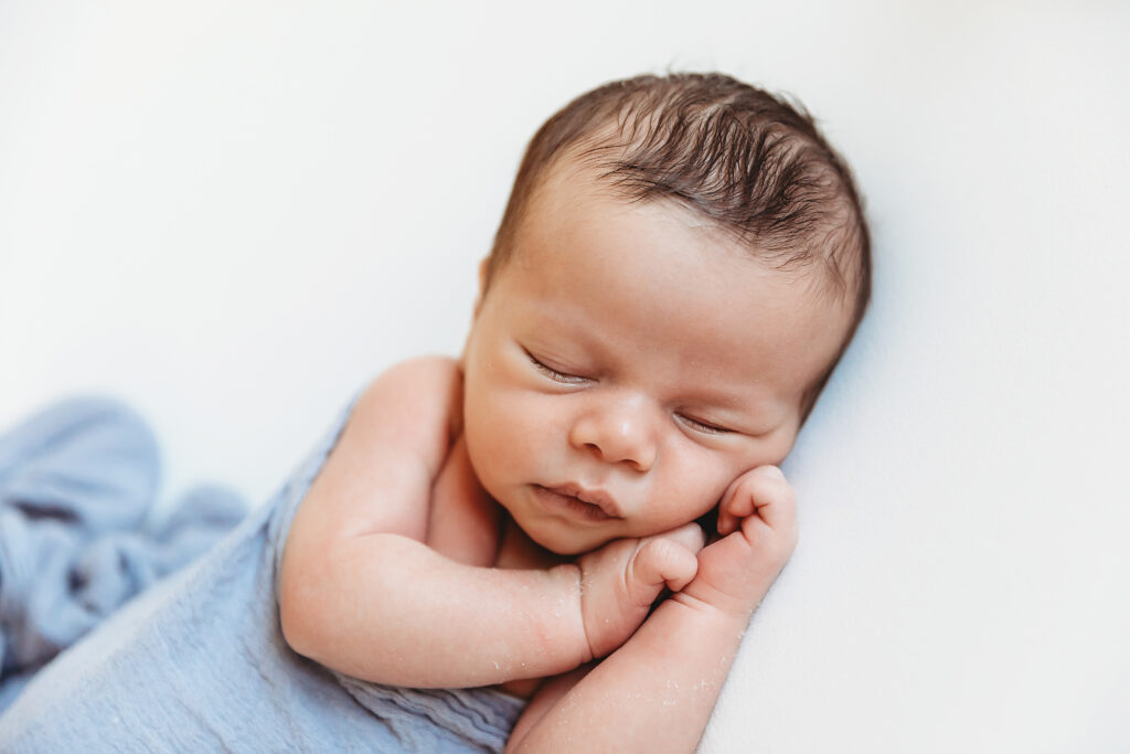 Side-lying pose with baby in soft blue wrap on white flokati with arms curled under chin at Reflection Images by Tracy Rowell in Florence SC