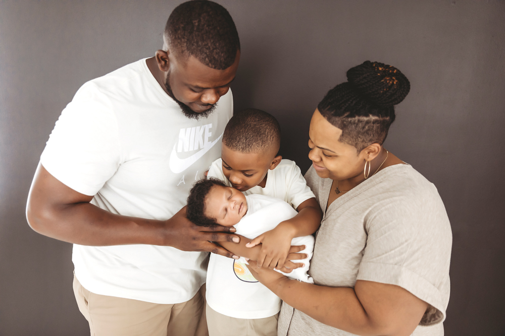 Close-up of family snuggled around swaddled Braylen on a warm-toned leather couch at Reflection Images by Tracy Rowell in Florence SC