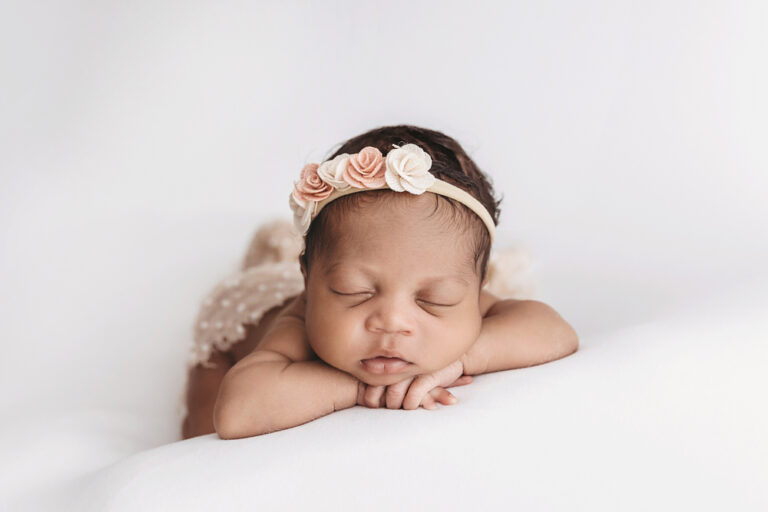 Newborn Harlem posed on her tummy with peach and cream floral crown, lace outfit showing against a soft white backdrop at Reflection Images by Tracy Rowell in Florence SC