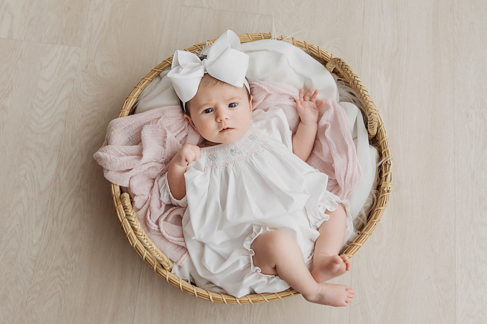 Mary Katherine lying in a round wicker basket with soft pink and white blankets in studio setting at Reflection Images by Tracy Rowell in Florence SC