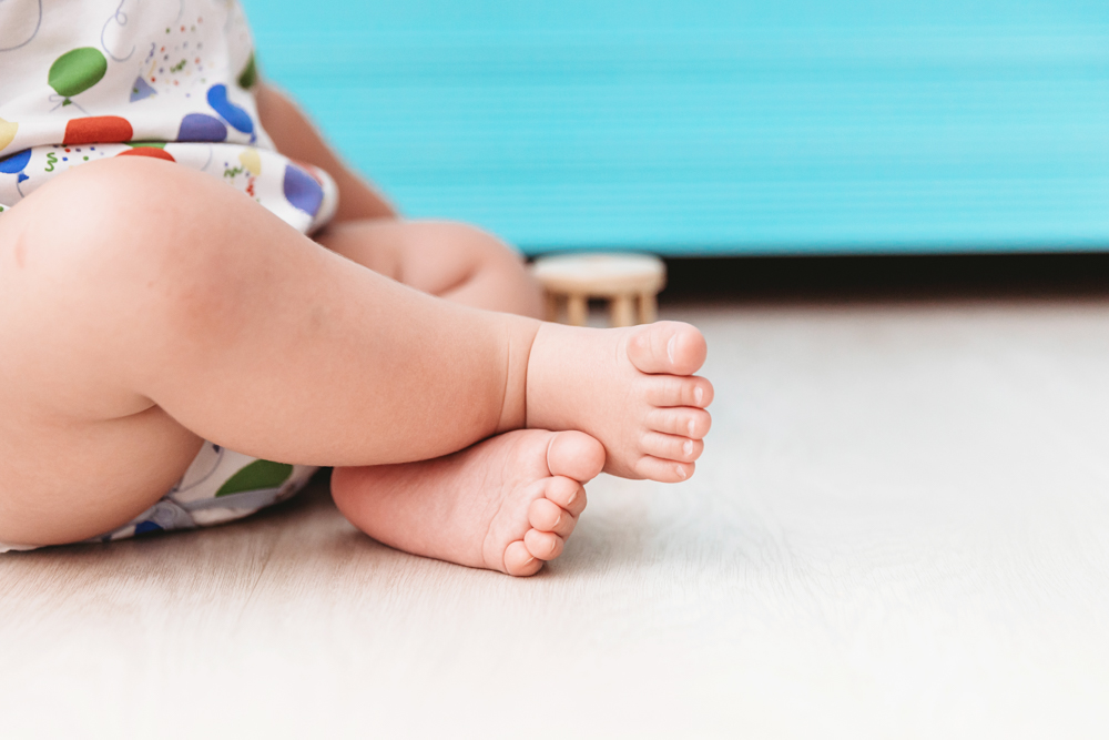 Macro close-up of Levis crossed toes in a balloon-print romper, seated on a wood floor with a blue background at Reflection Images by Tracy Rowell in Florence SC