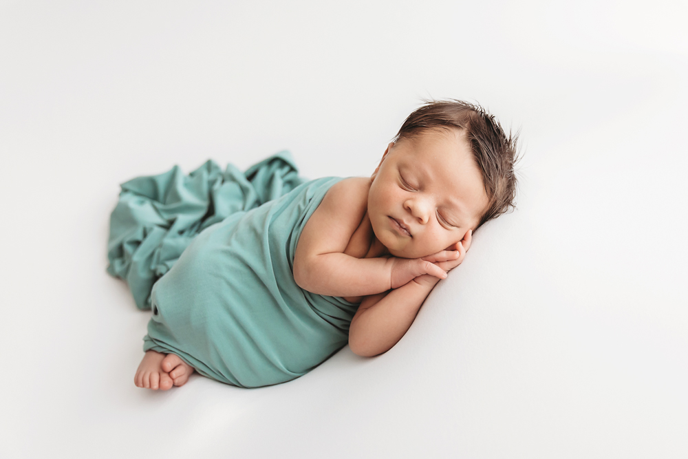 Newborn Liston in a sage wrap, posed on his side with hands folded under his cheek at Reflection Images by Tracy Rowell in Florence SC