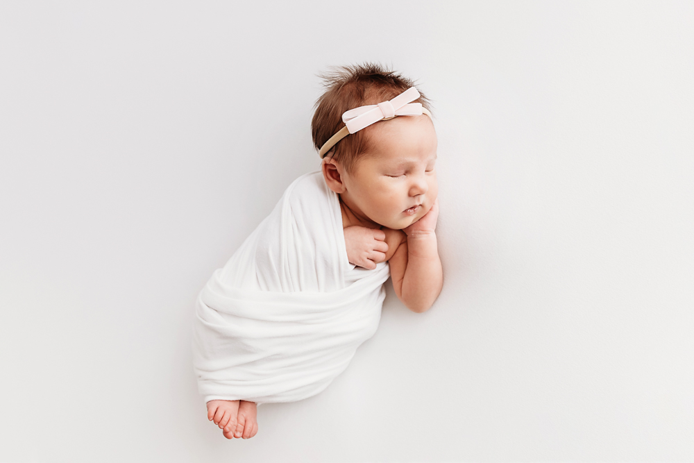 Newborn swaddled in white wrap with pink bow headband at Reflection Images by Tracy Rowell in Florence SC.