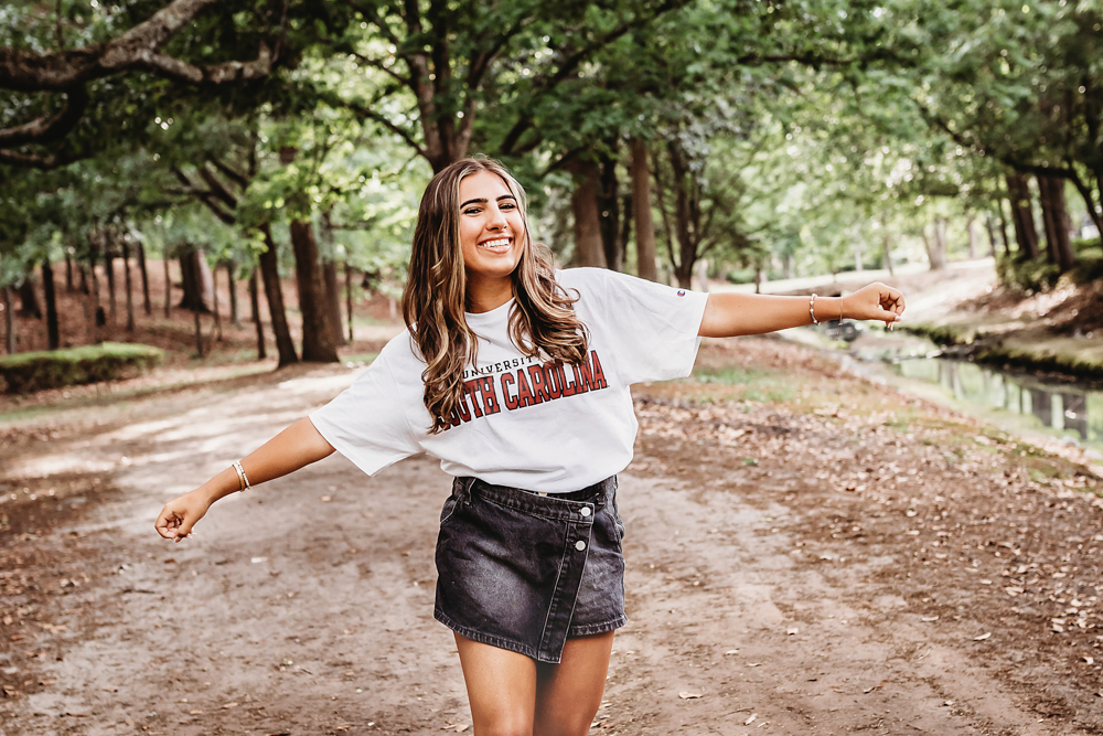 gravel path at golden hour, showing a twirling pose in USC shirt and denim skirt from a close-up angle at Reflection Images by Tracy Rowell in Florence SC.