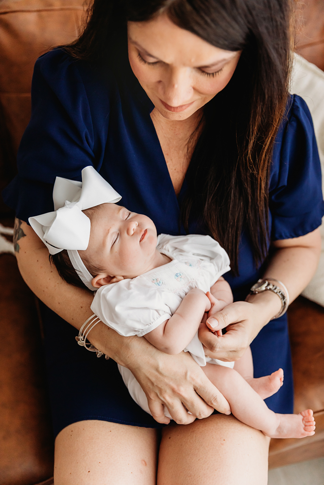 Mary Katherine resting on momas lap wearing a white outfit and oversized bow in studio light at Reflection Images by Tracy Rowell in Florence SC