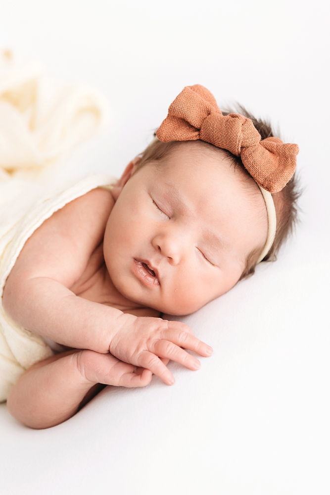 Close-up of baby resting in cream wrap with rust bow headband at Reflection Images by Tracy Rowell in Florence SC.