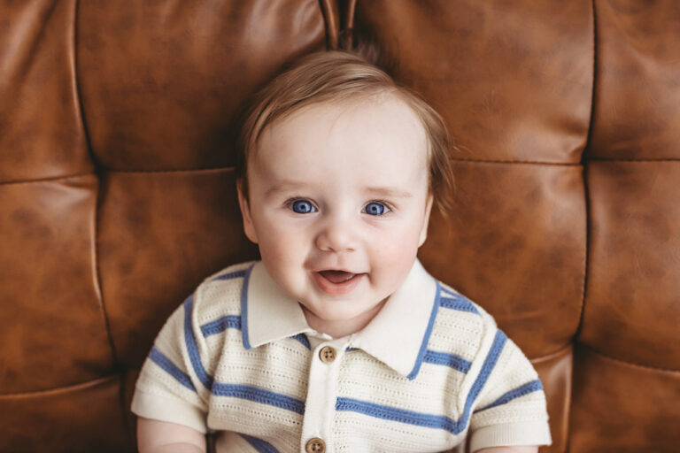 Baby boy smiling on leather couch in striped romper, milestone photographer Florence SC