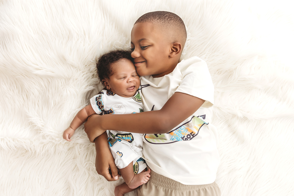 Sweet moment of big brother gently snuggling Braylen on leather couch, white swaddle and throw at Reflection Images by Tracy Rowell in Florence SC