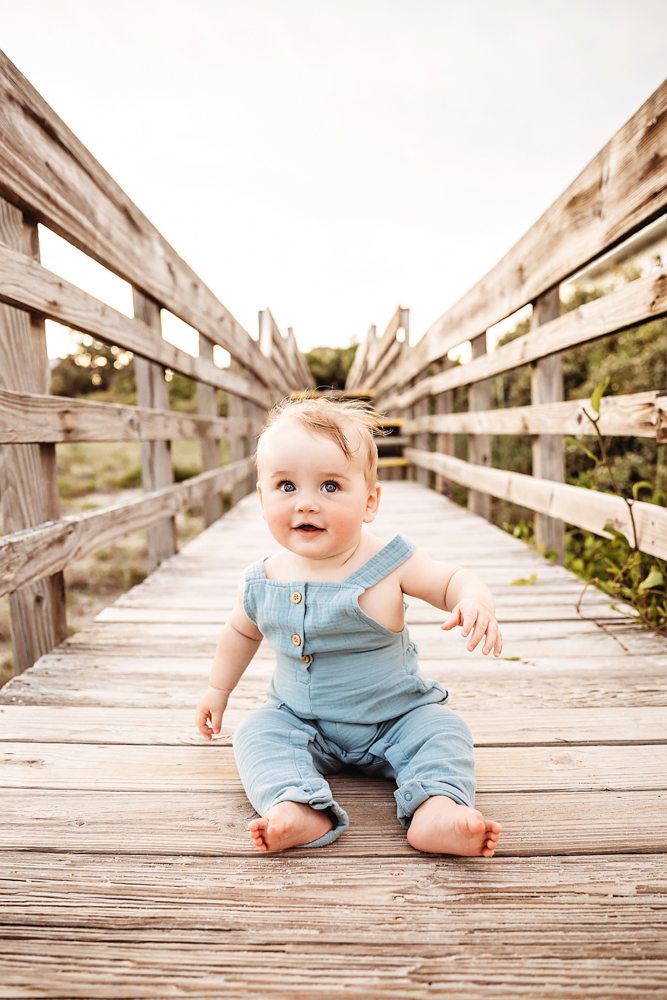 Cole sitting on a beach boardwalk in a soft blue romper with curious expression at Reflection Images by Tracy Rowell in Florence SC