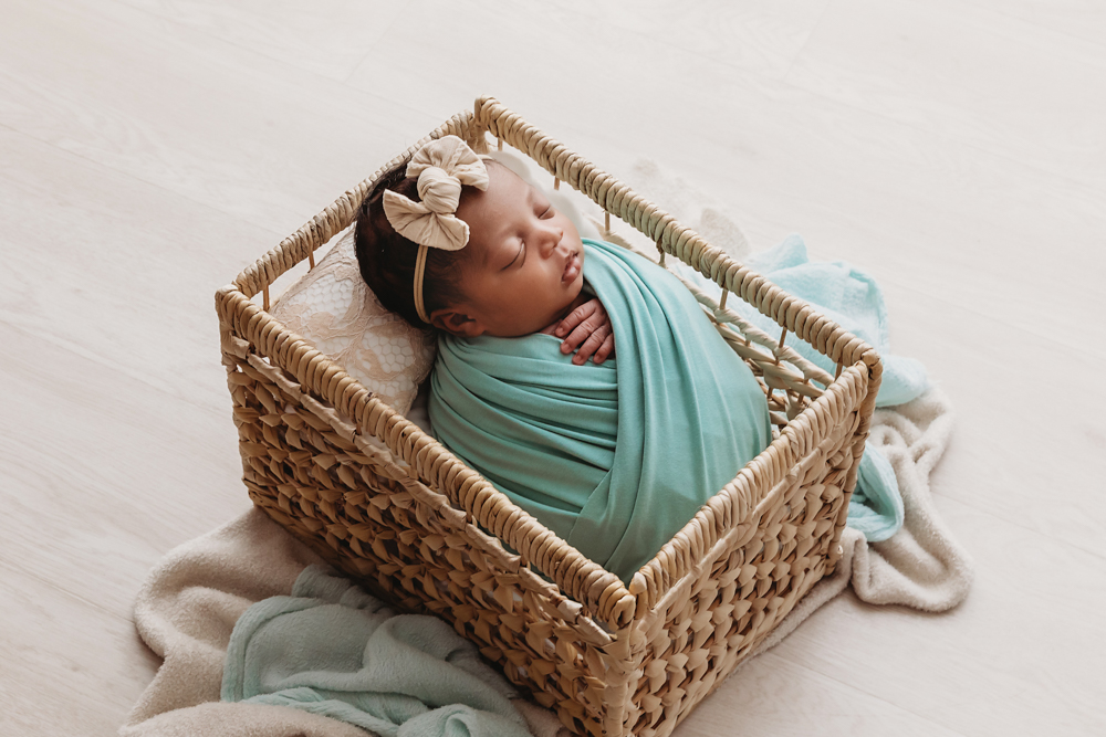 Side view of Harlem wrapped in teal with a cream bow headband, nestled in a square basket on neutral blankets at Reflection Images by Tracy Rowell in Florence SC