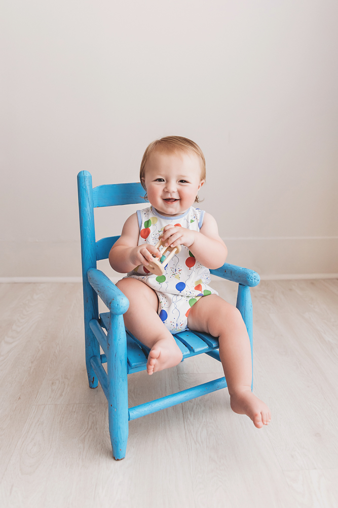 Levi smiling while holding a small toy, seated on a rustic blue wooden chair during his birthday milestone session at Reflection Images by Tracy Rowell in Florence SC