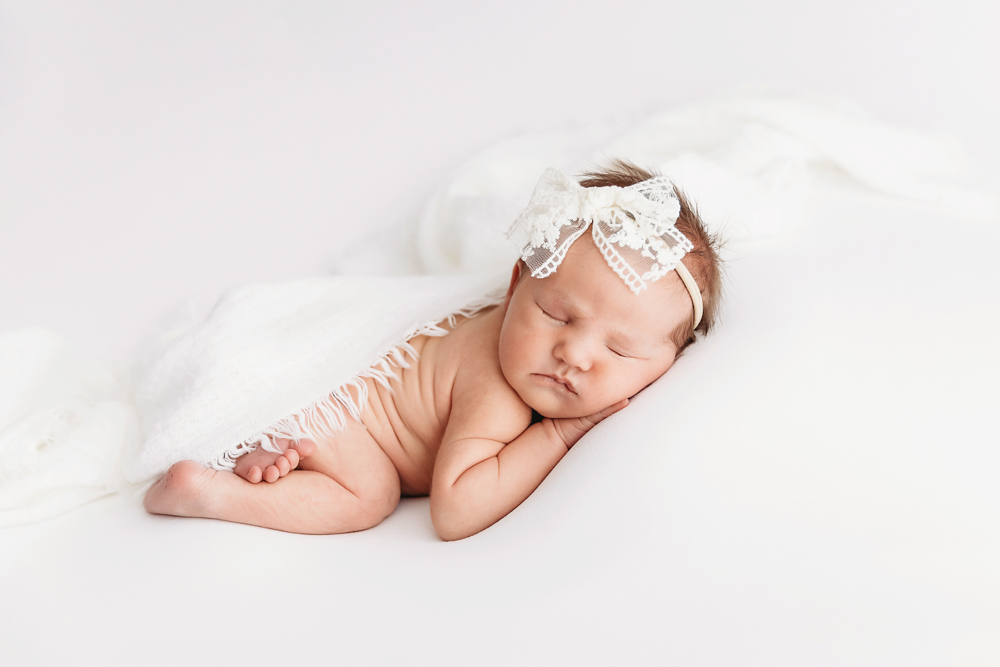 Baby sleeping on soft white blanket with lace bow headband at Reflection Images by Tracy Rowell in Florence SC.