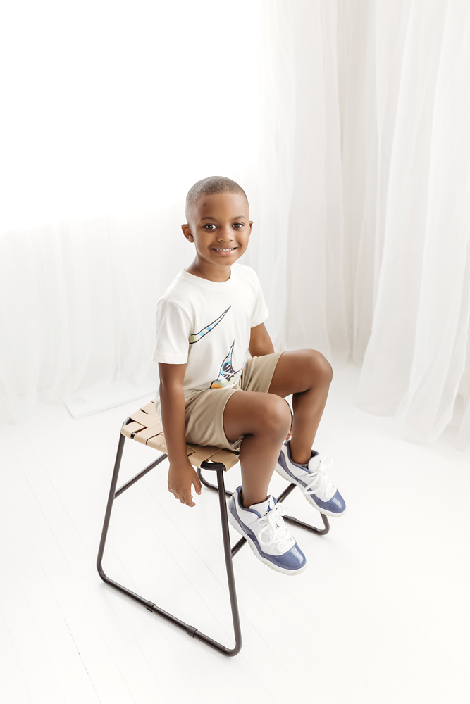 Playful sibling moment on white flokati rug, Braylen smiling in printed outfit next to laughing big brother at Reflection Images by Tracy Rowell in Florence SC