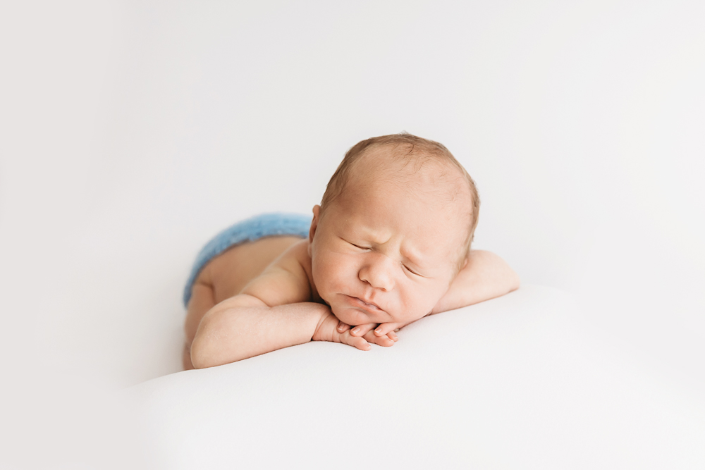 Newborn Harry posed bum-up in blue knit diaper cover against white backdrop at Reflection Images by Tracy Rowell in Florence SC