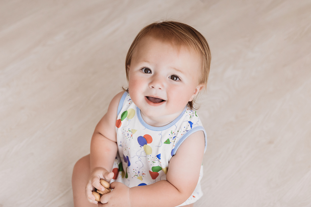 Close-up of Levi smiling warmly while seated on the wood floor, holding a toy in both hands at Reflection Images by Tracy Rowell in Florence SC