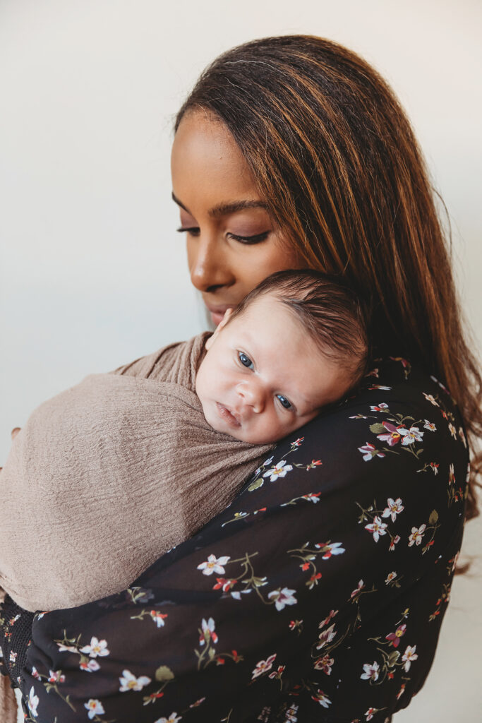 Mom holding newborn over shoulder with baby looking alert in soft light at Reflection Images by Tracy Rowell in Florence SC