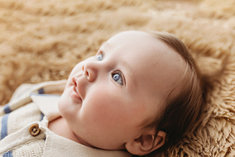 Baby boy looking up while lying on fuzzy tan blanket, photography studio near Florence SC