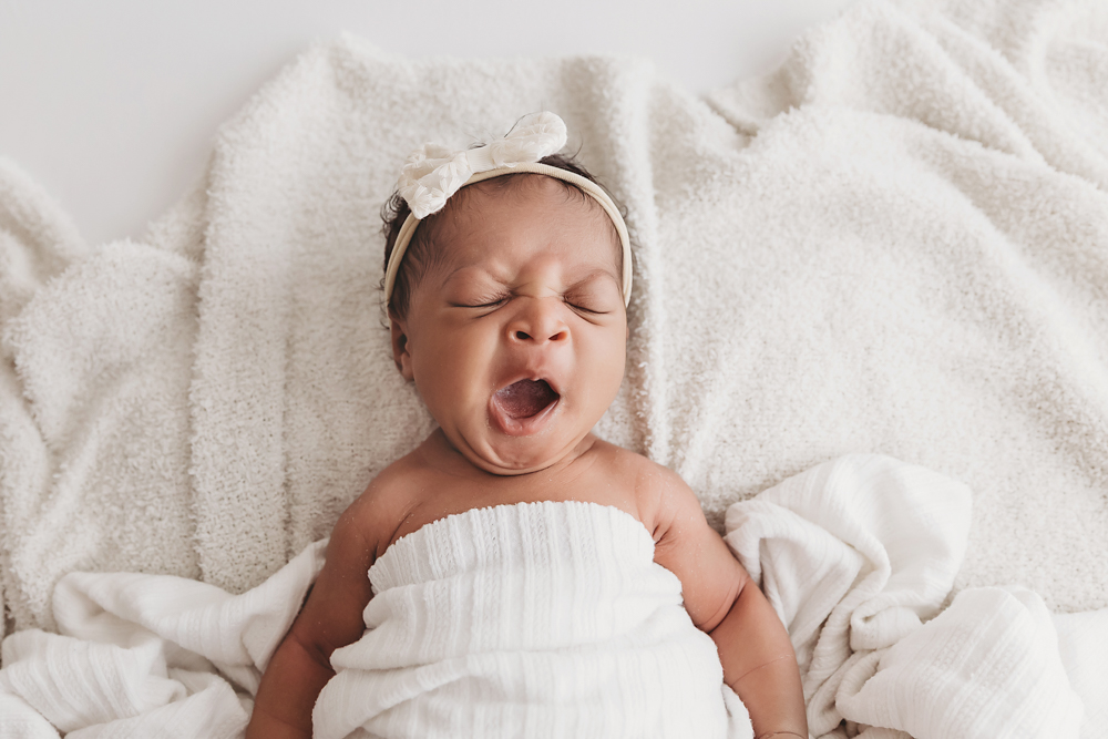 Adorable moment of Harlem yawning while lying on a white textured blanket with a cream bow headband at Reflection Images by Tracy Rowell in Florence SC