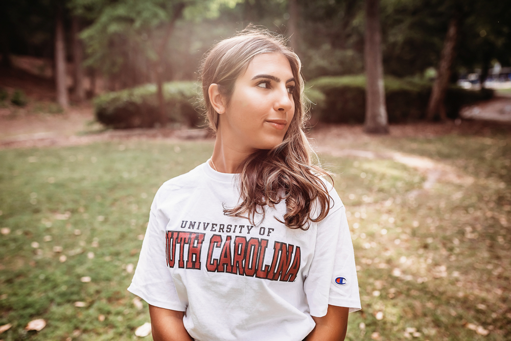 sunlit trail at golden hour, showing a looking-away pose in USC shirt and denim skirt from a close-up angle at Reflection Images by Tracy Rowell in Florence SC.