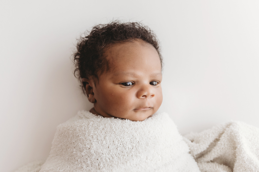 Bright-eyed Braylen swaddled in a soft, textured white wrap against a clean white background at Reflection Images by Tracy Rowell in Florence SC