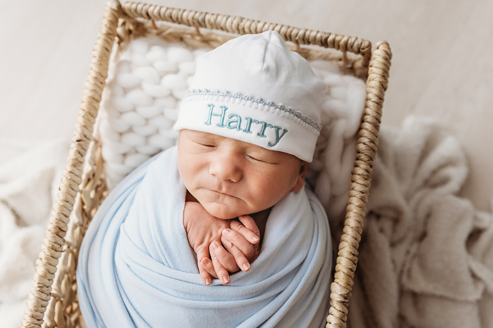 Harry swaddled in blue with matching hat embroidered with his name, resting in a wicker basket at Reflection Images by Tracy Rowell in Florence SC