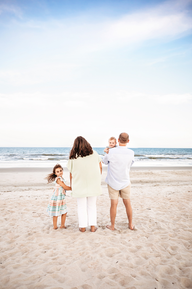 The Skinner family standing at the edge of the surf, back to camera, with Stella turning to smile at Reflection Images by Tracy Rowell in Florence SC