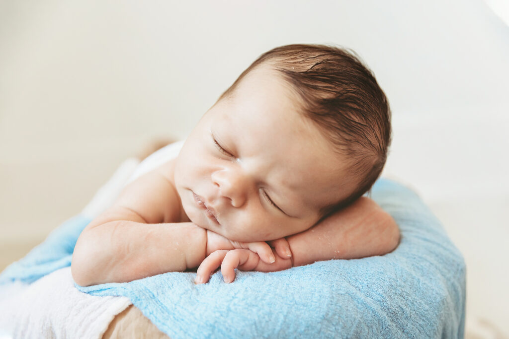 Newborn resting with head on folded arms, blue blanket base, softly lit in studio setting at Reflection Images by Tracy Rowell in Florence SC