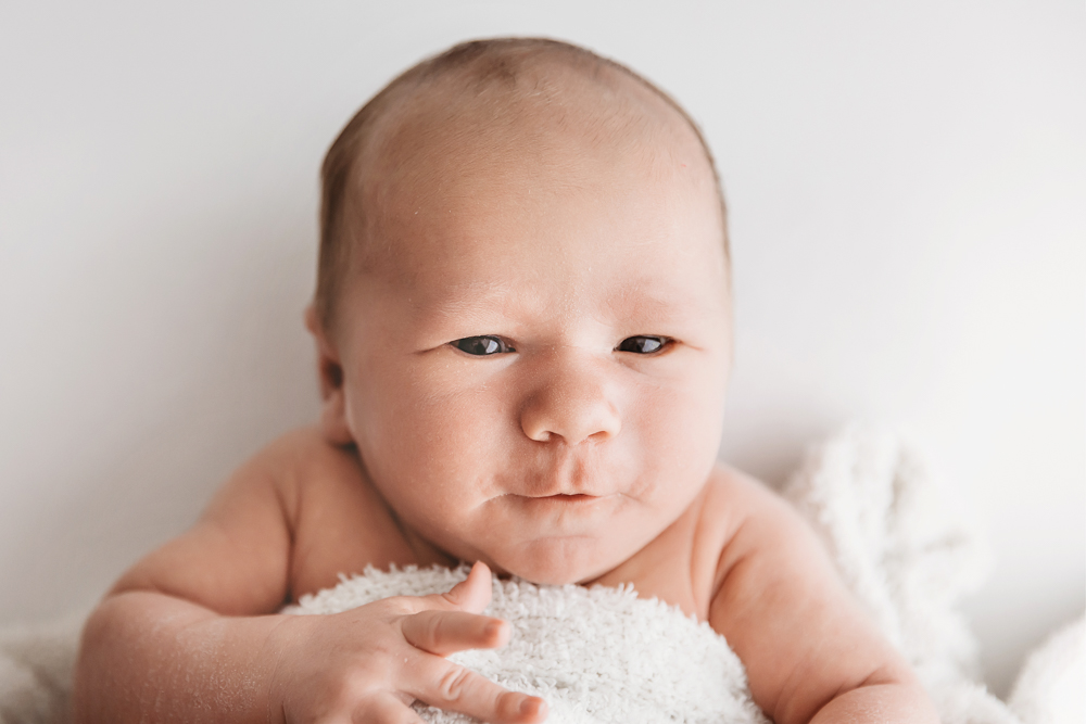 Newborn Harry with eyes open and puckered lips resting on a white textured blanket at Reflection Images by Tracy Rowell in Florence SC
