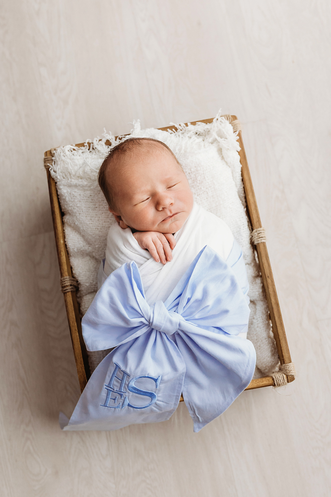 Swaddled baby Harry with large blue monogrammed bow resting in a wooden crate at Reflection Images by Tracy Rowell in Florence SC