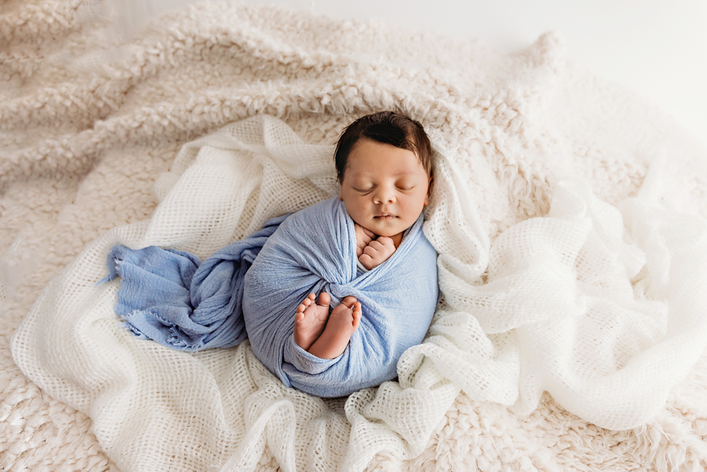 Newborn Liston wrapped in periwinkle blue swaddle and nestled in cream flokati layers at Reflection Images by Tracy Rowell in Florence SC