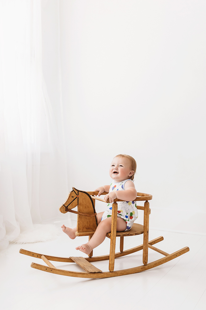 Levi laughing while riding a wooden rocking horse, legs raised in joy with soft natural light pouring in at Reflection Images by Tracy Rowell in Florence SC