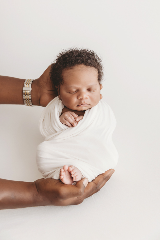 Braylen wrapped in white and cradled gently in adult hands with tiny feet forward at Reflection Images by Tracy Rowell in Florence SC