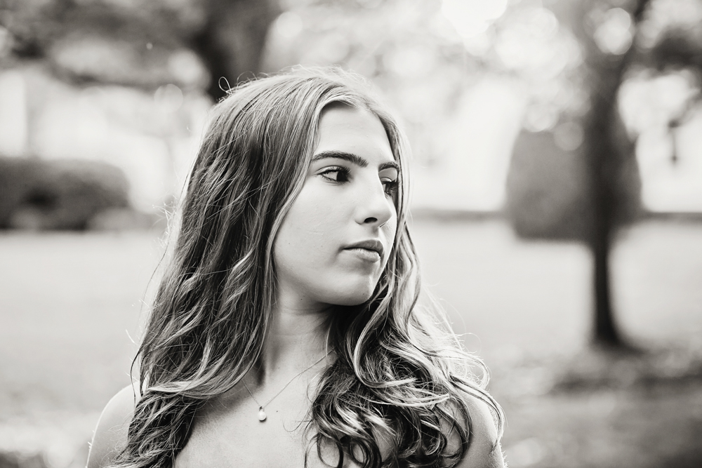 black-and-white-Senior session photo taken in gravel path at golden hour, showing a looking-away pose in white boots from a over-the-shoulder angle