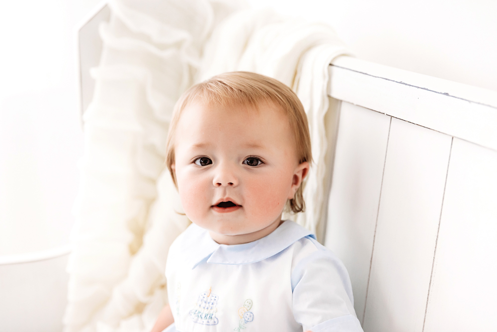 Close-up of Levi sitting near a soft ruffled blanket, gazing calmly in his embroidered blue birthday outfit at Reflection Images by Tracy Rowell in Florence SC